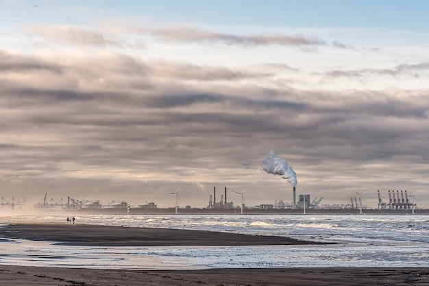 Kostenloses Foto schöner schuss eines meeres mit windmühlen und fabrik in der ferne unter einem bewölkten himmel