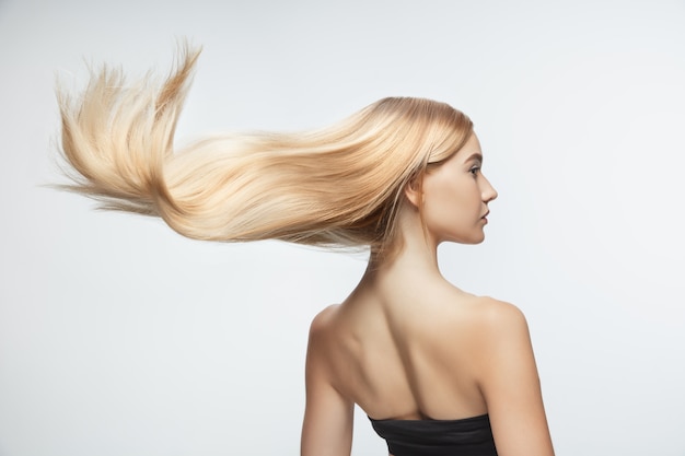 Kostenloses Foto schönes modell mit langen glatten, fliegenden blonden haaren lokalisiert auf weißem studiohintergrund. junges kaukasisches modell mit gepflegter haut und haaren, die auf luft blasen.