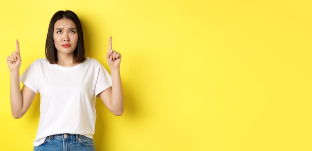 Kostenlose Foto schönheits- und modekonzept schöne asiatische frau in weißem t-shirt, die mit dem finger nach oben zeigt und über y steht