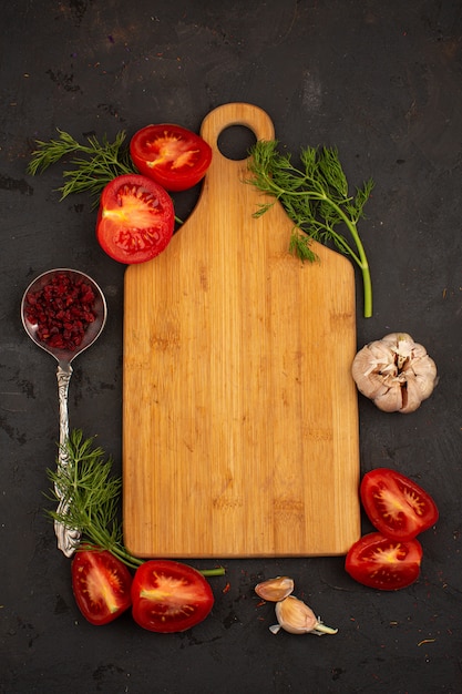 Kostenloses Foto schreibtischgemüse geschnittene reife frische tomaten und gemüse mit knoblauch auf einem dunklen boden