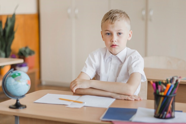 Schüler, der mit den Händen auf Schreibtisch im Klassenzimmer sitzt