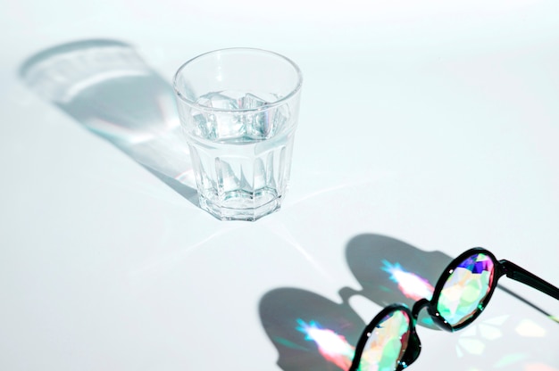 Kostenloses Foto schwarze sonnenbrille mit mehrfarbenlinse und glas wasser mit schatten auf weißem hintergrund