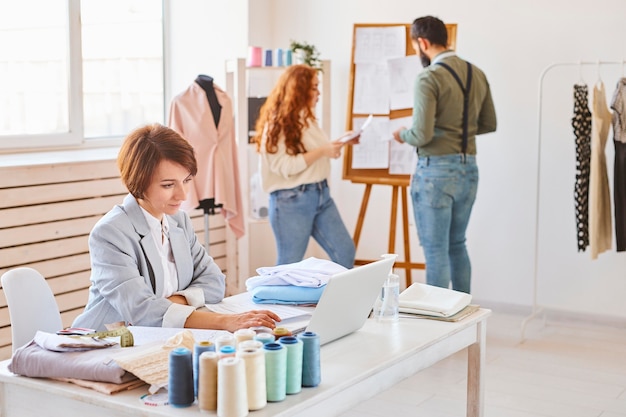 Kostenlose Foto seitenansicht der modedesignerin, die im atelier mit kollegen und laptop arbeitet