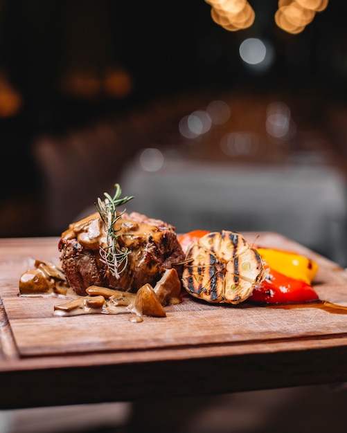 Kostenloses Foto seitenansicht von gegrilltem rindfleisch, serviert mit pilzen gegrilltem gemüse und sauce auf einem holzbrett