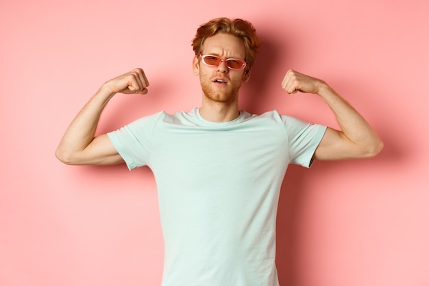 Kostenloses Foto selbstbewusster junger mann mit roten haaren, der eine sommersonnenbrille und ein t-shirt trägt und einen starken und fitten...