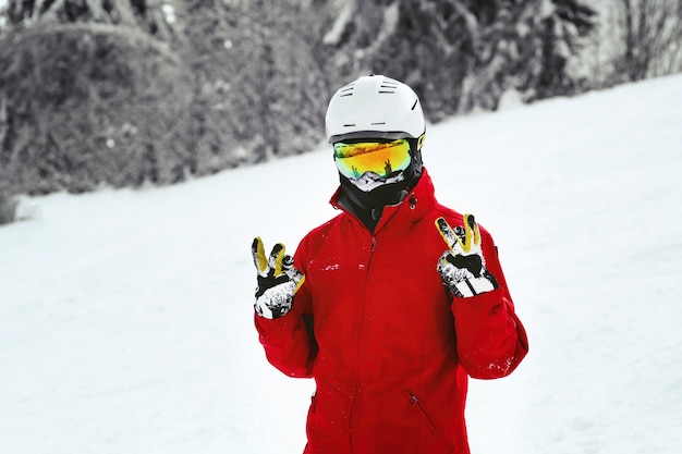 Kostenloses Foto snowboarder in der roten jacke, im weißen sturzhelm und in den gelben gläsern wirft auf dem hügel auf