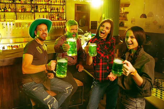 St. Patrick's Day Party. Glückliche Freunde feiern und trinken grünes Bier. Junge Männer und Frauen tragen grüne Hüte. Pub Interieur.