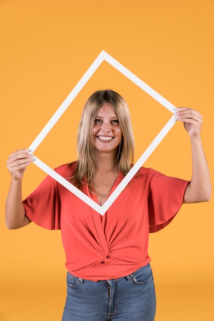 Stilvolle Frau, die weißen Grenzfotorahmen vor ihrem Gesicht hält