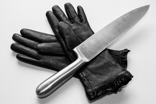 Überkopfaufnahme eines Metallmessers über schwarzen Handschuhen auf einer weißen Oberfläche