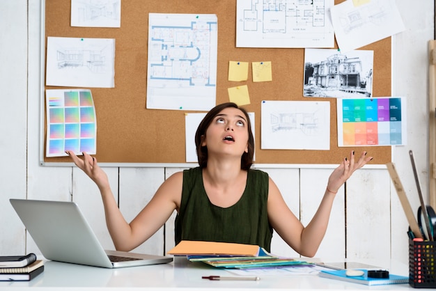 Kostenloses Foto verärgerte junge schöne geschäftsfrau gestikulierend, am arbeitsplatz sitzend