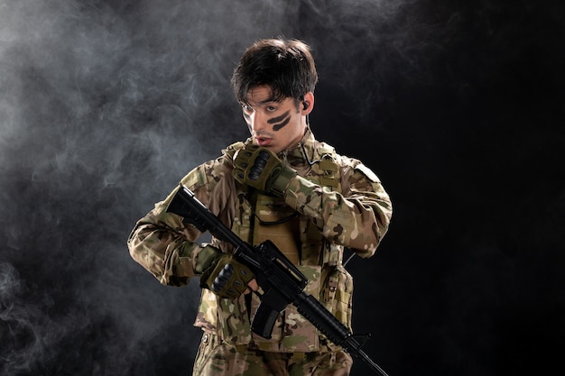 Kostenloses Foto vorderansicht eines männlichen soldaten in tarnung, der auf eine schwarze wand zielt