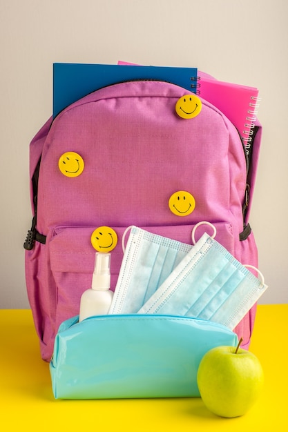 Kostenloses Foto vorderansicht kinderschultasche mit heftenspray und masken auf gelbem schreibtisch