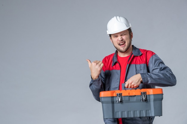 Kostenloses Foto vorderansicht männlicher baumeister in uniform mit werkzeugkoffer auf grauem hintergrund