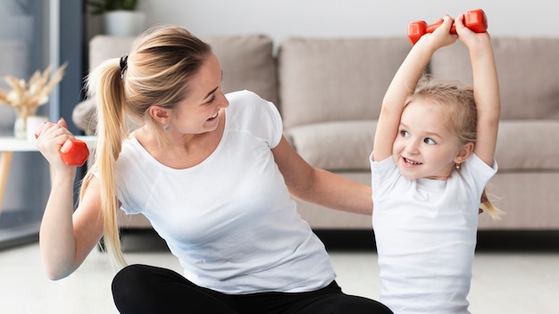 Vorderansicht von Mutter und Tochter, die mit Gewichten zu Hause trainieren