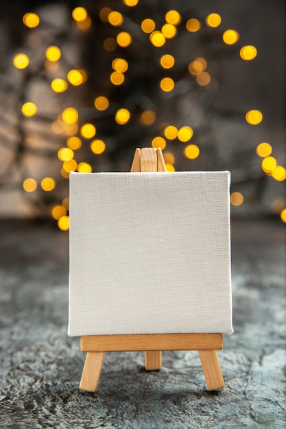 Vorderansicht weiße Leinwand auf Holz Staffelei Weihnachtslichter auf dunklem Hintergrund