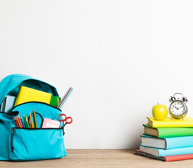 Wecker auf Stapel Büchern und gut verpackter Schultasche mit Versorgungen