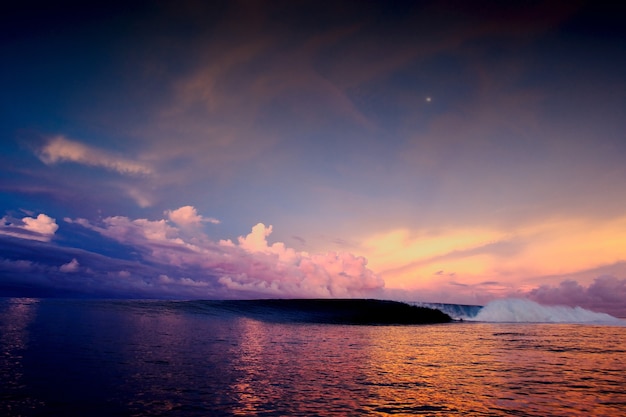 Weitwinkelaufnahme eines hypnotisierenden Sonnenuntergangs im Ozean unter einem Himmel voller bunter Wolken