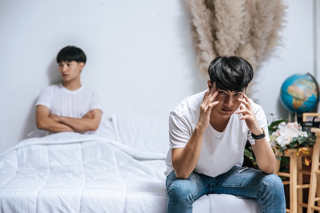 Kostenlose Foto zwei junge männer waren wütend auf dem bett und der andere saß am rand des bettes und war gestresst.