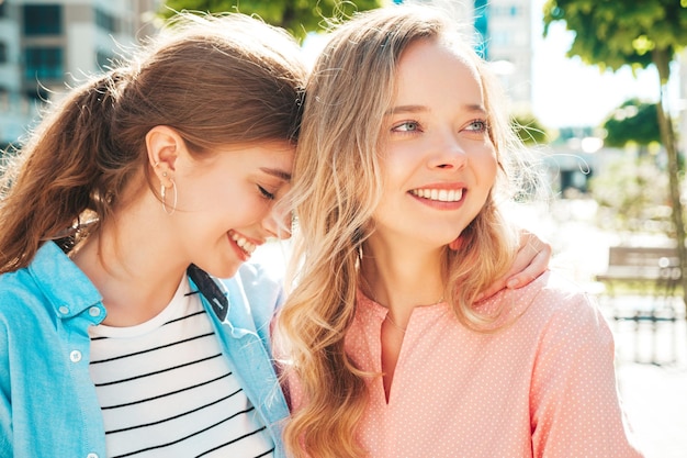 Kostenloses Foto zwei junge schöne lächelnde hipster-frauen in trendiger sommerkleidung und dresssexy unbeschwerte frauen posieren auf dem straßenhintergrund positive reine models, die sich bei sonnenuntergang amüsieren, umarmen und verrückt werden