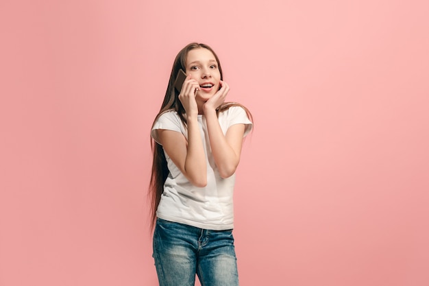 A adolescente feliz em pé e sorrindo contra a parede rosa