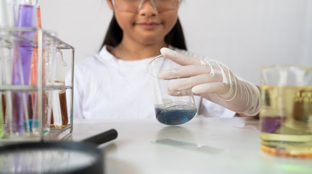 Foto adorável jovem de óculos e luvas de segurança está segurando frascos de química enquanto faz cientista.