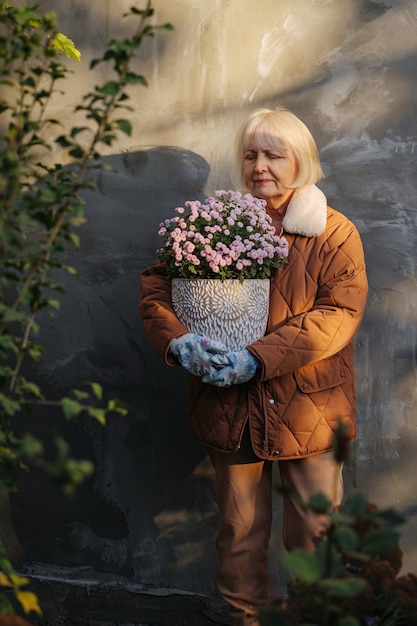 Foto älteres weibchen mit blumen an einem sonnigen frühlingstag. ältere frau in oberbekleidung mit topfblumen