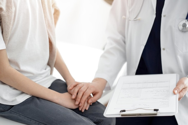 Foto arzt und kind-patient. der arzt hält die schreibtafel in der hand und beruhigt einen jungen. das konzept der idealen gesundheit in der medizin