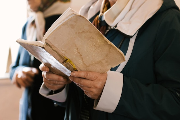 As mãos de uma mulher idosa estão segurando um velho livro de orações na igreja