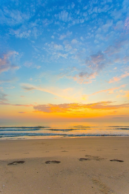 Foto as pegadas foram mostradas na areia em vista do mar e do pôr do sol com céu azul