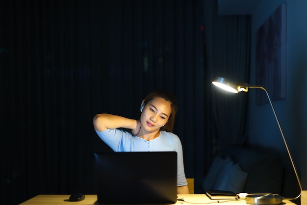 Asiatische Frauen sind faul, während sie lange Stunden vor einem Computer in der späten Nacht im Wohnzimmer zu Hause arbeiten.