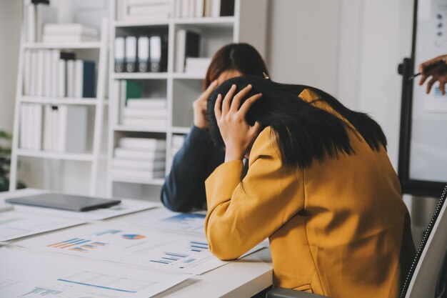 Foto asiatische frauen sind gestresst, während sie am laptop arbeiten. müdige asiatische geschäftsfrau mit kopfschmerzen im büro fühlt sich krank bei der arbeit.