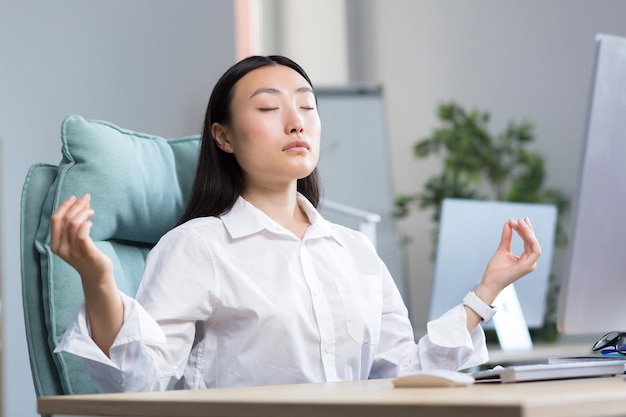 Foto asiatische geschäftsfrau, die im büro arbeitet, ruht und meditiert und macht atemübungen, um sich zu beruhigen