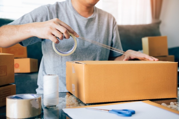 Foto asiatische unternehmer-teens verwenden das klebeband, um die schachtel zu versiegeln, indem sie das produkt verpacken, um es an die kunden zu schicken