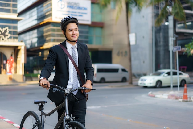 Asiatischer Geschäftsmann, der sein Fahrrad morgens von zu Hause aus schiebt und sich darauf vorbereitet, mit dem Fahrrad zur Arbeit zu fahren. Öko-Transport.