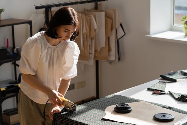 Foto atelier geschäftsinhaberin schneiderin designerin arbeit im studio schnittmaterial für muster mit cutter