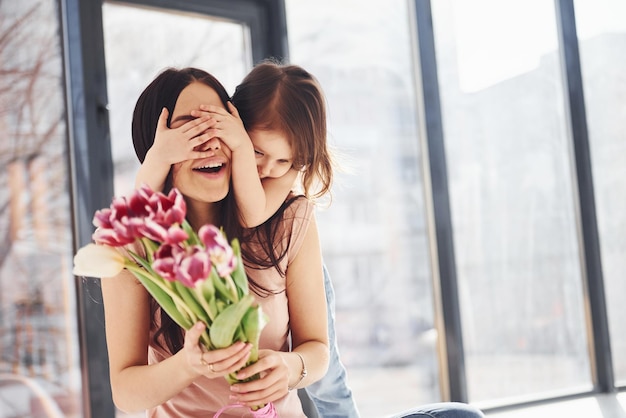 Foto augen zudecken tochter gratuliert mutter zum urlaub und gibt blumenstrauß