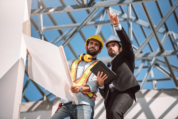 Bauingenieur und Bauarbeiter-Manager mit digitalem Tablet und Blaupausen Sie suchen nach dem Teamwork-Konzept für die Zusammenarbeit in der nächsten Bauphase