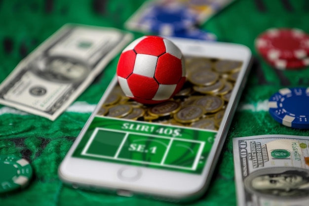 Foto bola de futebol equilibrada em um smartphone com fichas de cassino e notas de dólar conceito de apostas esportivas