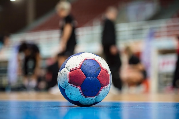 Bola de handebol no chão da quadra Árbitros desfocados treinadores e atletas e fundo do campo