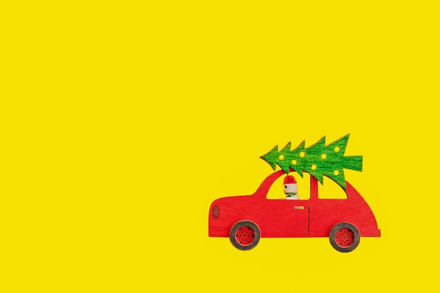 Brinquedo carro vermelho de madeira com árvore de Natal no telhado e boneco de neve ao volante em fundo amarelo