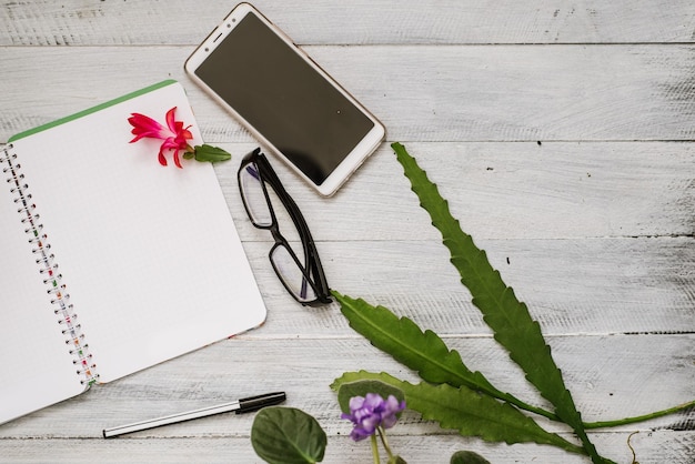 Caderno de papel aberto com páginas em branco e smartphone entre muitas plantas no fundo branco de madeira. Copie o espaço, flatlay