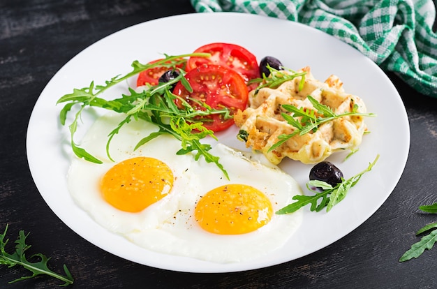 Café da manhã com waffles de abobrinha, ovos fritos, tomate, azeitonas pretas e rúcula em fundo branco. Aperitivos, lanche, brunch. Comida vegetariana saudável.