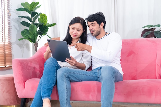 Casal asiático sentado no sofá com tablet pc comemorando vitórias on-line ou sucesso nos negócios em casa espaço livre Cônjuges millennials desfrutando de grande venda na loja virtual