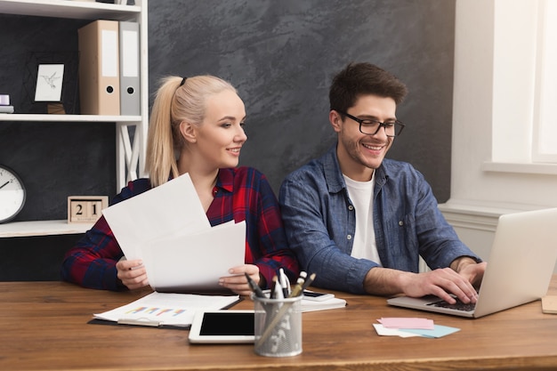 Casal feliz de jovens colegas trabalhando em um escritório moderno. Dois colegas de trabalho discutindo seu trabalho, trabalhando com documentos e digitando no laptop, copie o espaço