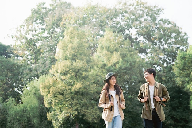 Foto casal sorridente andando com mochilas sobre fundo natural.