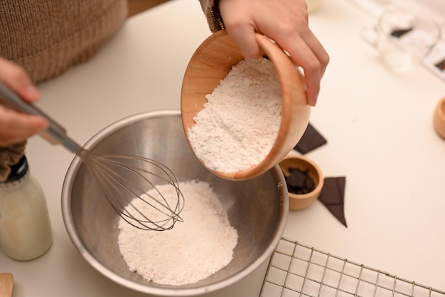 Chef feminino derramando uma xícara de farinha em uma tigela preparando os ingredientes dos biscoitos