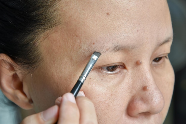 Close-up de mulher asiática aplicando maquiagem com pincel de sobrancelha