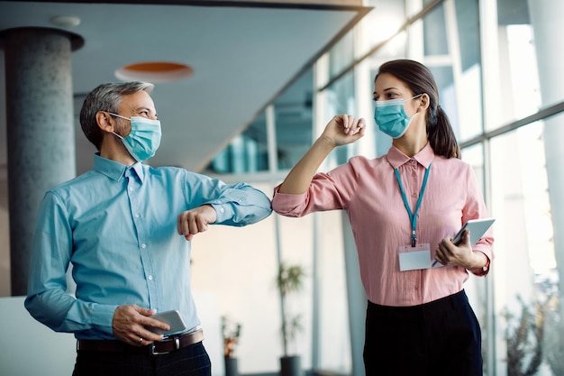 Colegas felizes cumprimentando com cotovelos em um corredor durante a pandemia de coronavírus