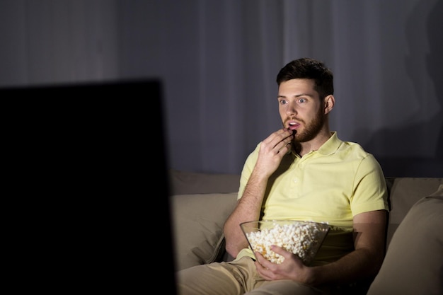 Foto conceito de pessoas, meios de comunicação de massa, televisão e entretenimento - jovem assistindo tv e comendo pipoca à noite em casa