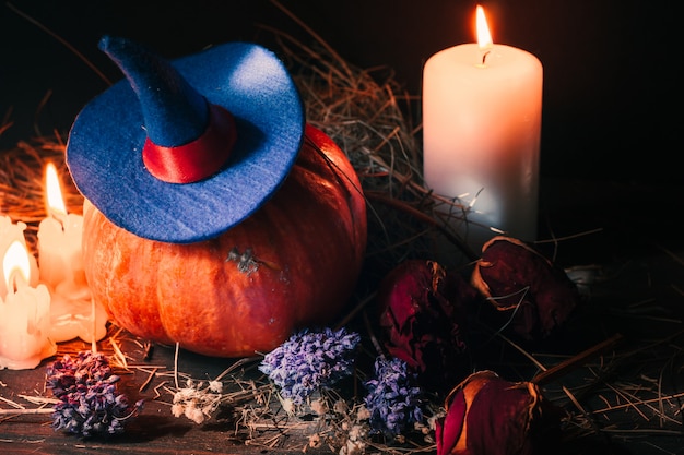 Decoração festiva de Halloween com abóbora laranja com chapéu de bruxa, velas, rosas e feno seco.